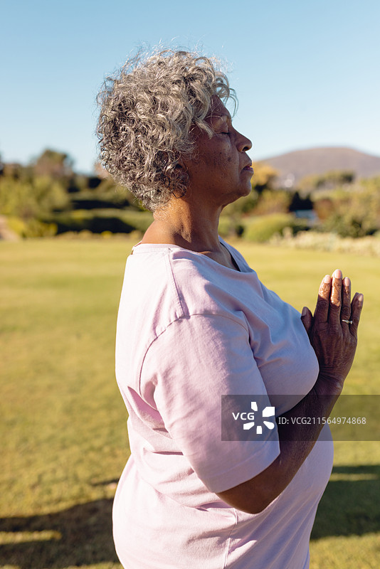在草地上冥想的老年女性，双手合十，展示着银色戒指。图片素材