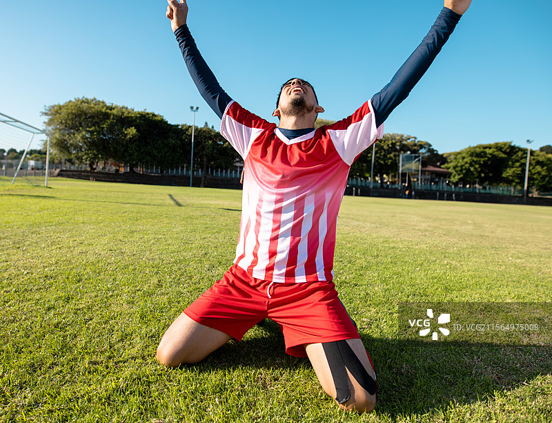 青少年男孩跪在足球场的球门旁，庆祝进球，膝盖上贴着胶带。图片素材