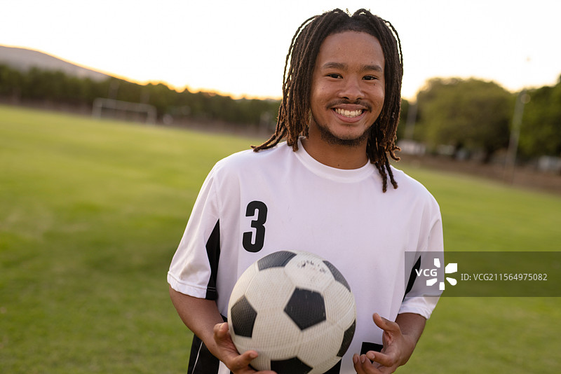 在日落时分，穿着白色3号球衣的男子站在足球场上，手里拿着足球，留有空白空间。图片素材