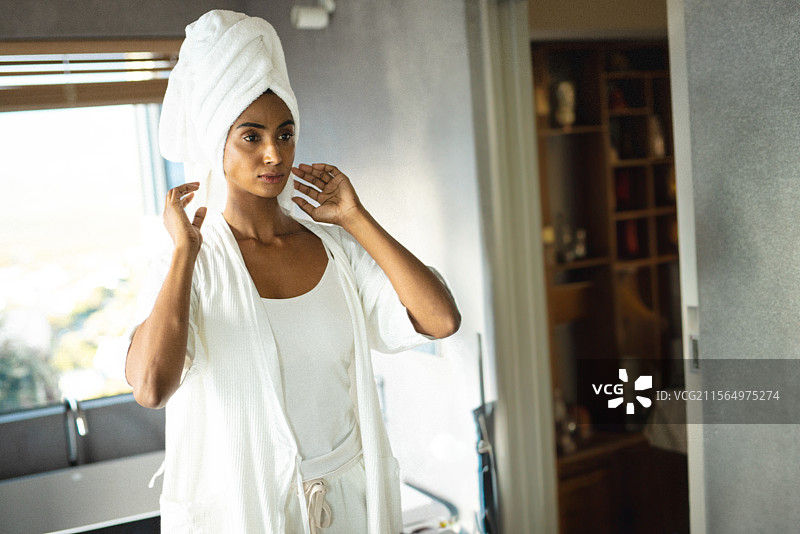 印度亚洲女性在明亮的浴室中调整头发上的毛巾，身穿浴袍，窗帘拉上。图片素材