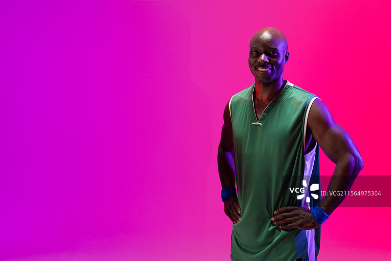 一位非裔美国男性在摄影棚中摆姿势，穿着绿色篮球球衣和蓝色腕带，留有空白空间。图片素材