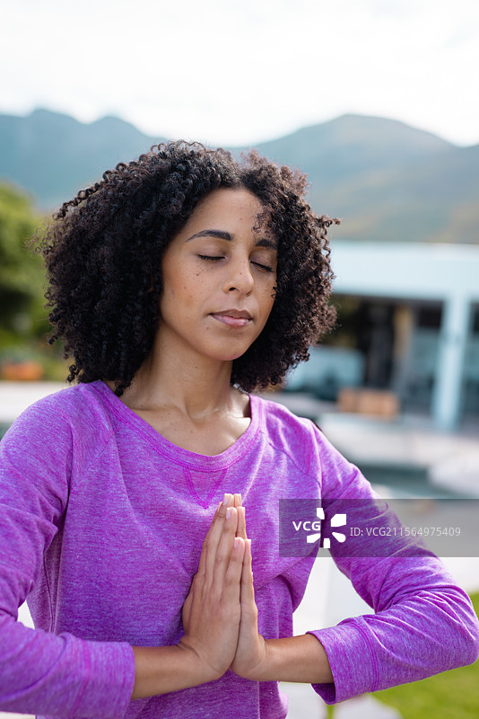 中年女性在现代住宅的泳池边露台上练习瑜伽，俯瞰山脉。图片素材
