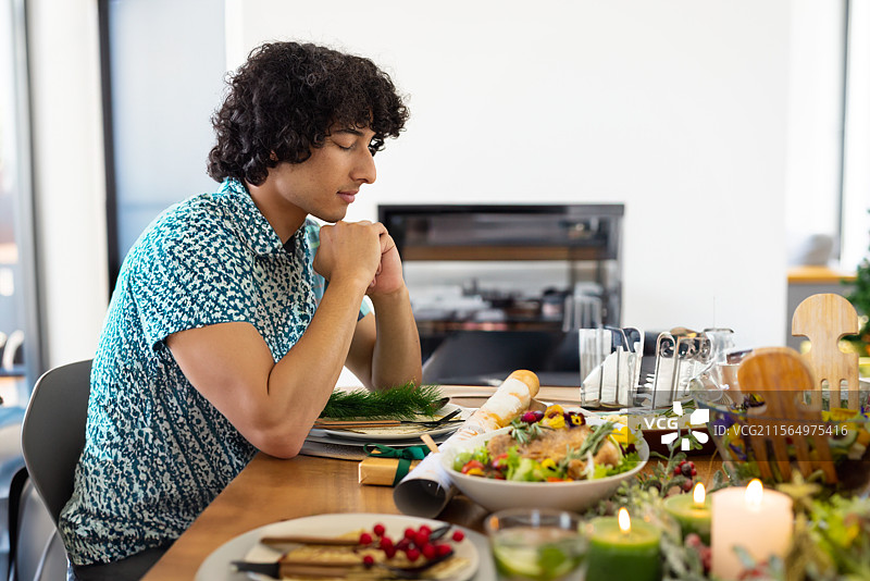 年轻男子坐在家中的木餐桌旁，桌上有沙拉碗和蜡烛，留有空白空间图片素材