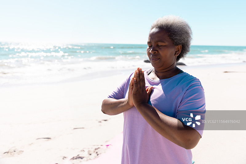 一位年长的非裔美国女性在沙滩水边练习冥想，寻找内心的平静图片素材