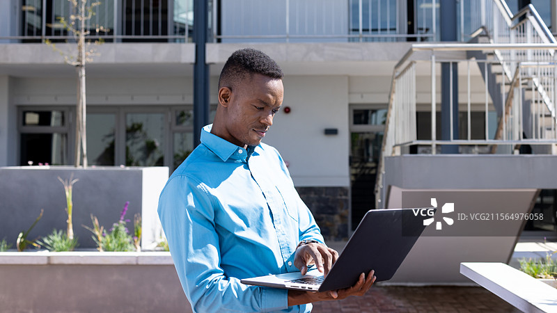 中年非裔美国男性在户外庭院的混凝土花箱旁使用笔记本电脑打字图片素材