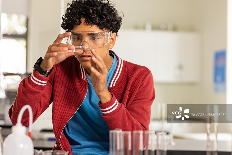 少年在科学实验室检查玻璃小瓶，旁边有试管和挤压瓶。图片素材