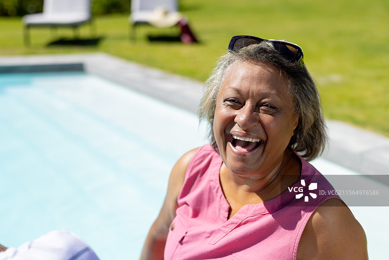 放松的老年女性在后院泳池边享受阳光，戴着太阳镜，留有空白空间图片素材