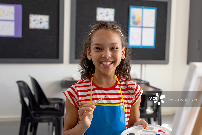 多种族的学龄女孩在学校的艺术教室里绘画，手持调色板和画笔图片素材