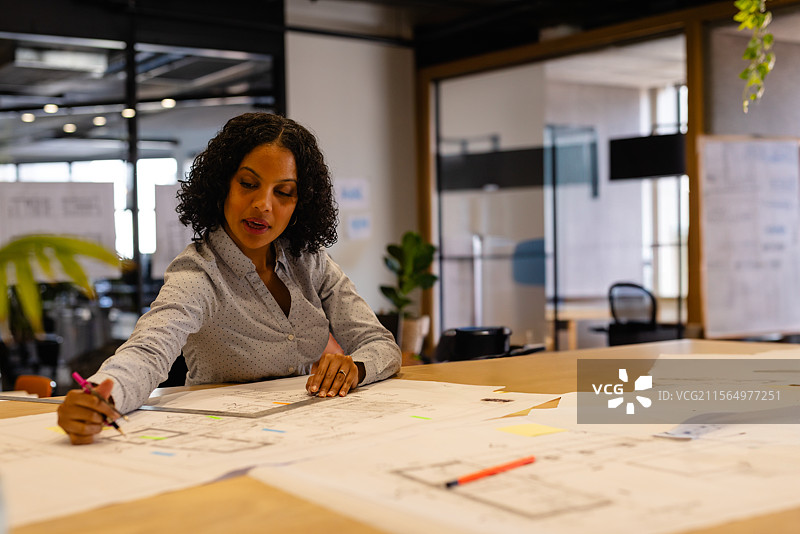 女性在办公室的木桌上用粉色笔标记建筑蓝图，研究布局。图片素材