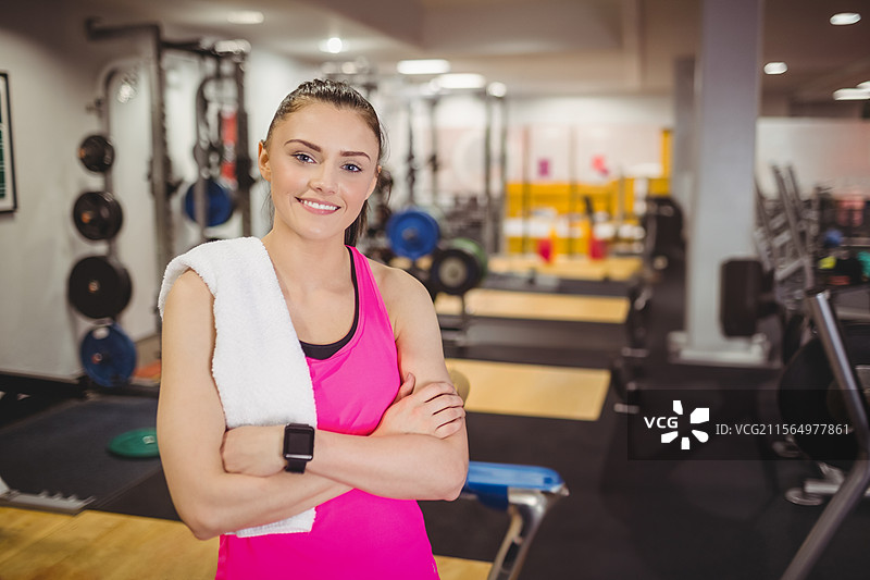 年轻女性在健身房双臂交叉，手持毛巾，佩戴智能手表。图片素材