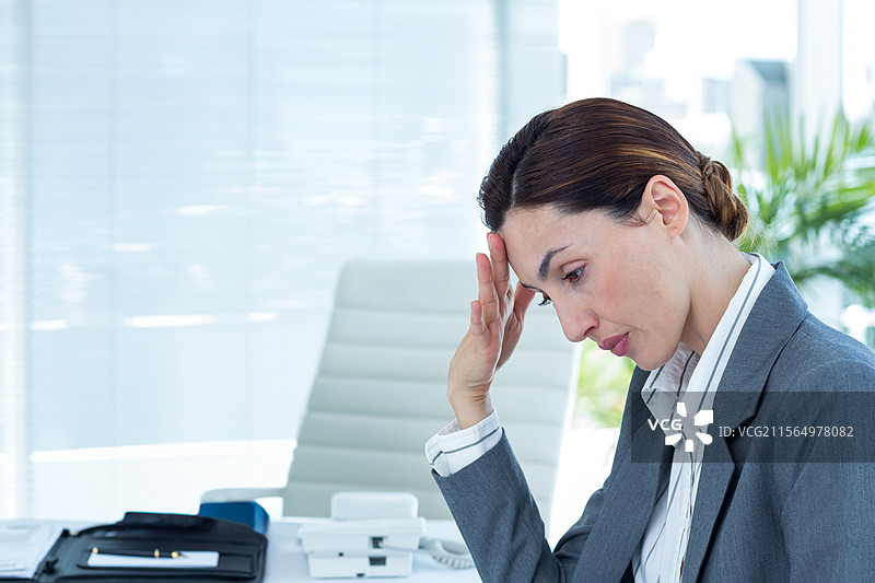 中年女商人在办公室桌前坐着，头靠在手上，旁边有电话和文件，留有空白空间图片素材