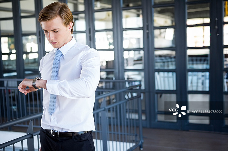 商人在玻璃墙的办公室大堂查看模拟腕表，精准掌握时间。图片素材