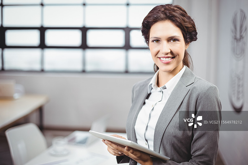 微笑的女商人在会议室里拿着平板电脑，桌子上有咖啡杯，留有空白空间图片素材