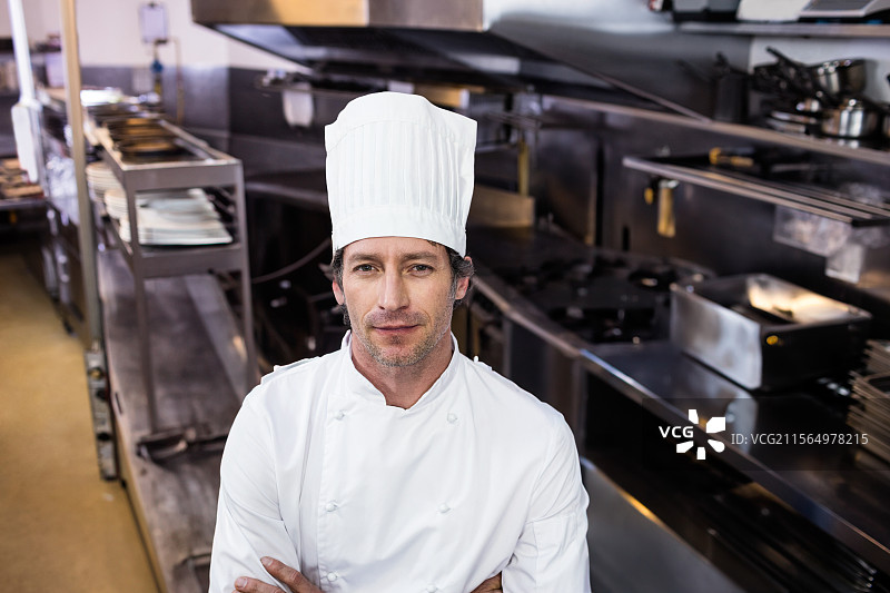穿着外套和帽子的男厨师，在配备钢制烤箱和炉灶的商业厨房工作图片素材