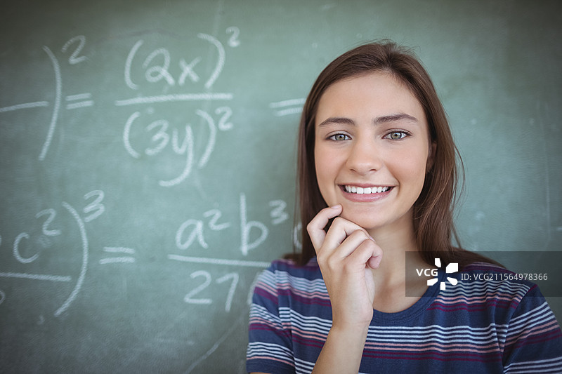 一名女学生在教室里站着，身后是大型数学公式黑板，留有空白空间。图片素材