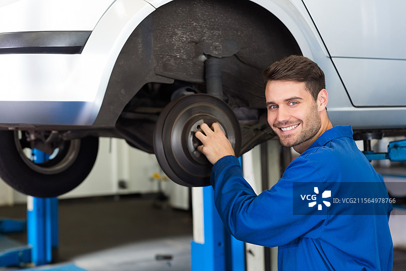 中年男性机械师在车库内检查汽车的刹车鼓，旁边有升降柱，留有空白空间图片素材