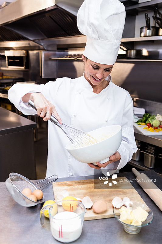 成熟的女性厨师在商业厨房中搅拌面糊，旁边有蛋壳和擀面杖图片素材