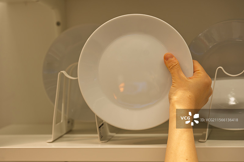 手拿白色盘子放入橱柜图片素材