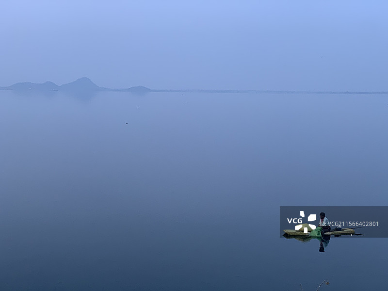 在印度特伦甘纳邦卡里姆纳加尔的湖面上划皮划艇的男子与天空相映。图片素材