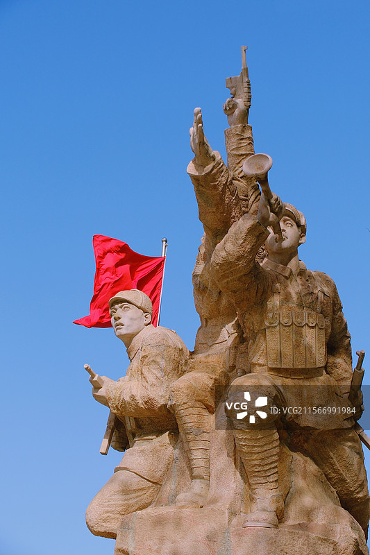 蓝色天空背景下飘扬的红旗和红军战士雕塑。国旗。烈士雕像。烈士陵园图片素材