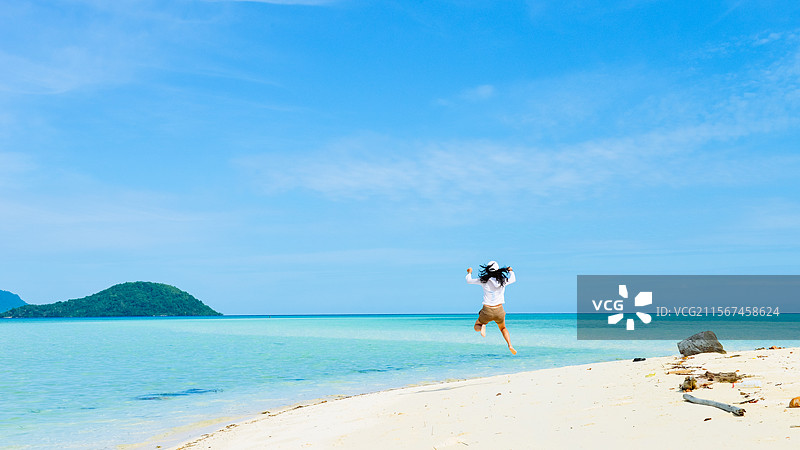 年轻亚洲女性在马来西亚沙巴仙本那的军舰岛的白沙滩上开心运动跳跃图片素材