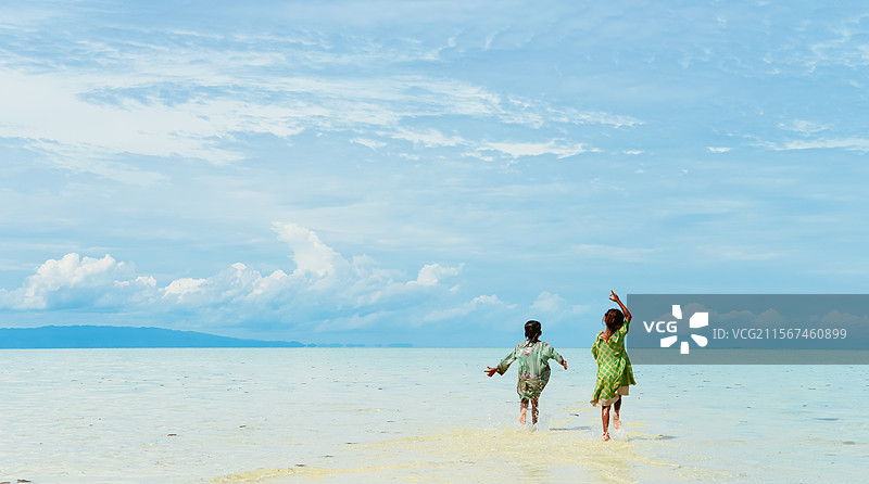 两个巴瑶族（Bajau）小女孩在马拉西亚沙巴仙本那军舰岛的潮水中跑向天际线图片素材