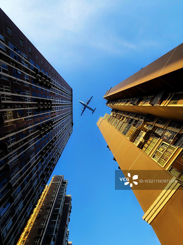 《城隙·天际飞影》在城市的缝隙间仰望，高楼如卫士般矗立两旁。一架飞机划破澄澈蓝天，似是奔赴远方的梦。图片素材