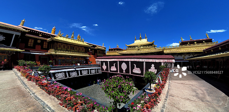 西藏拉萨大昭寺金顶在蓝天映衬下熠熠生辉红墙庄重古朴殿前繁花似锦尽显藏传佛教寺院的庄严与绚丽。图片素材