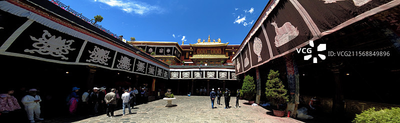 西藏拉萨大昭寺金顶在蓝天映衬下熠熠生辉红墙庄重古朴殿前繁花似锦尽显藏传佛教寺院的庄严与绚丽。图片素材