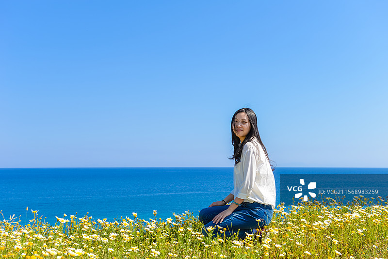 一位亚洲女性在希腊圣托里尼岛开满鲜花的海滩边欣赏春季海景图片素材