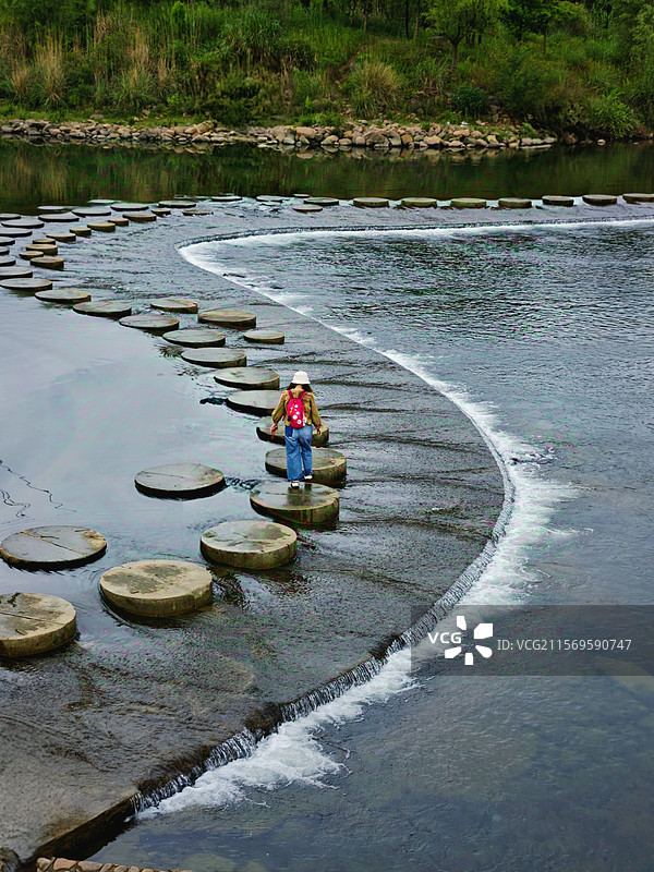 溪上石径周日和朋友来富阳龙鳞坝，她走到石头上红色背包成了聚焦点，S型的石径和水流有了延伸感图片素材