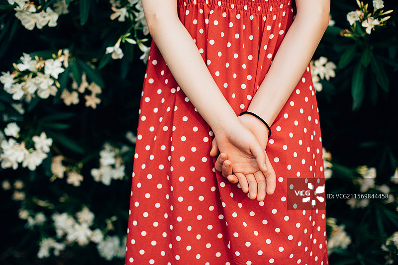 盛开的夹竹桃花丛旁，少女身着波点红裙双手背在身后，局部特写图片素材