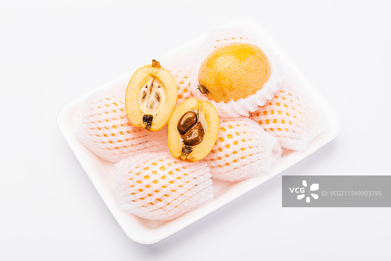 白色餐盒上泡沫网套装着新鲜枇杷果实与切开一半的成熟果肉特写图片素材