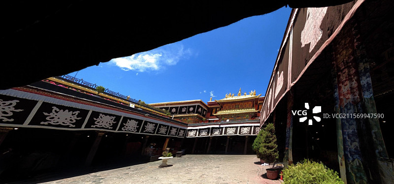 西藏拉萨大昭寺金顶在蓝天映衬下熠熠生辉红墙庄重古朴殿前繁花似锦尽显藏传佛教寺院的庄严与绚丽。图片素材