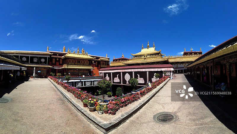 西藏拉萨大昭寺金顶在蓝天映衬下熠熠生辉红墙庄重古朴殿前繁花似锦尽显藏传佛教寺院的庄严与绚丽。图片素材