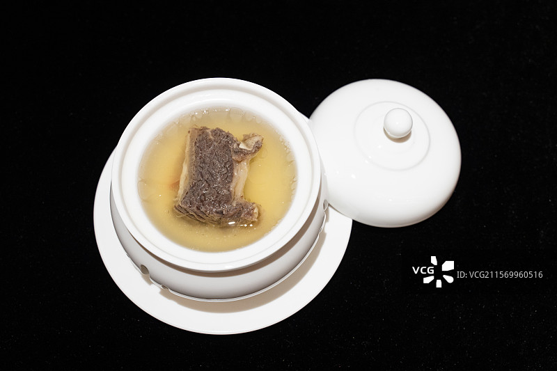 黑色背景白色餐具里的一段排骨和汤料图片素材