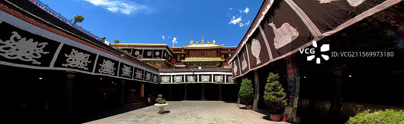 西藏拉萨大昭寺金顶在蓝天映衬下熠熠生辉红墙庄重古朴殿前繁花似锦尽显藏传佛教寺院的庄严与绚丽。图片素材