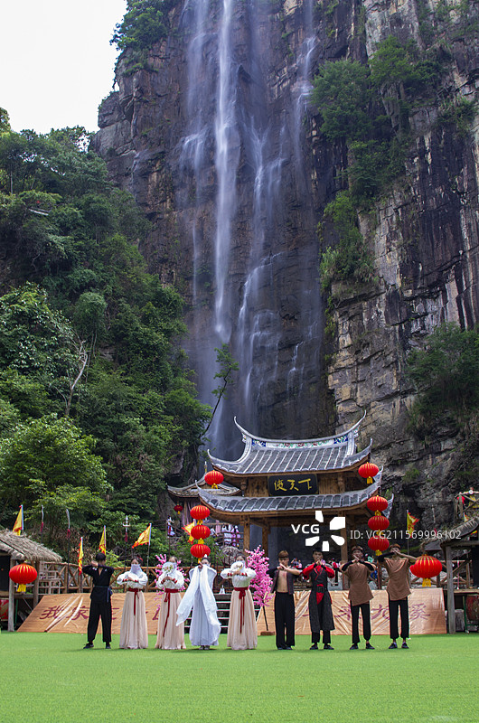 侠天下千尺瀑布下侠天下木质牌坊前的电影情景演出广场上九位演员抱拳向游客观众们致意图片素材
