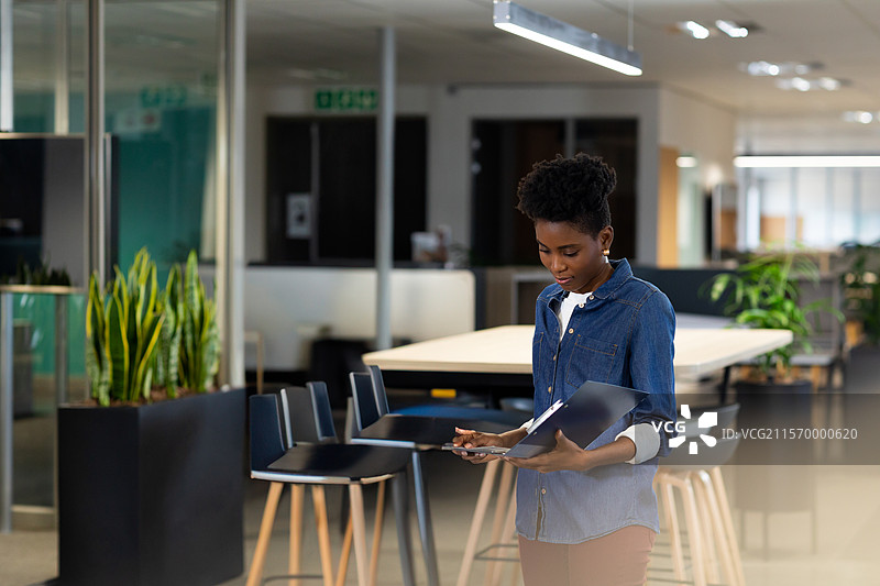 非裔美国女性在现代办公室的桌子上检查文件，手持文件夹，留白空间图片素材