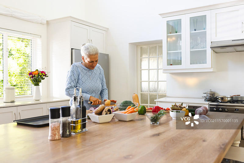 老年女性在家厨房的木岛上切菜，旁边有砧板和刀，留有空白空间。图片素材