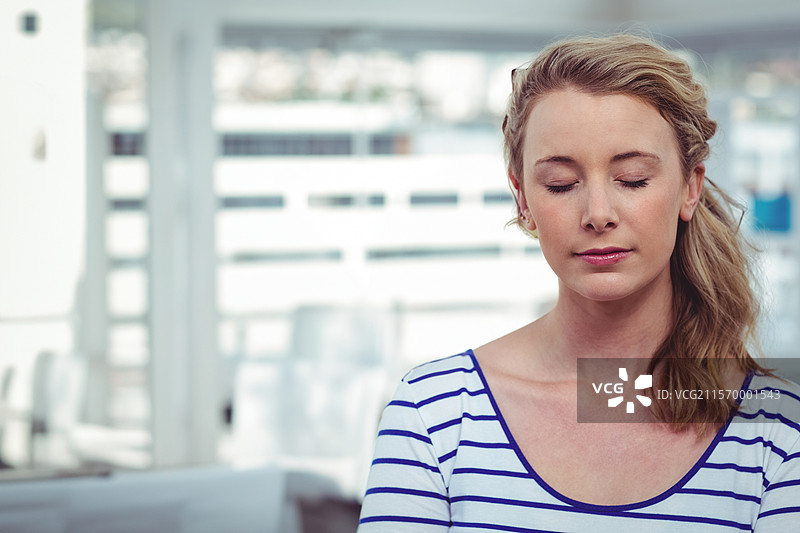 在明亮的工作室内坐着冥想的女性，穿着条纹衬衫，留有空白空间图片素材