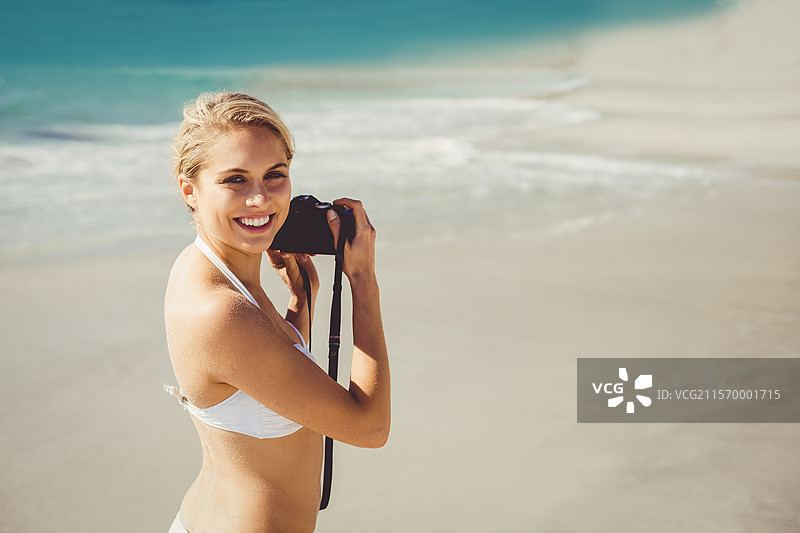 女性摄影师在沙滩上用单反相机拍摄海滩场景，背景是碧蓝的海浪。图片素材