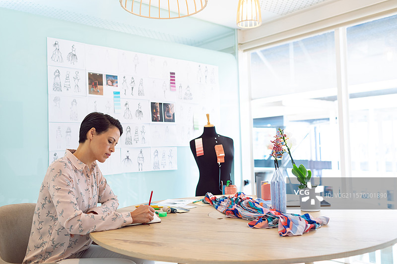 素描纸和布料碎片散落在浅蓝色设计工作室的圆形木桌上图片素材