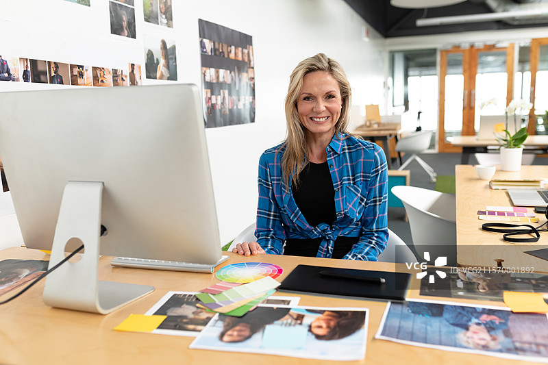 在工作室的桌子上，职业女性正在整理照片和色卡，旁边有一台绘图板。图片素材