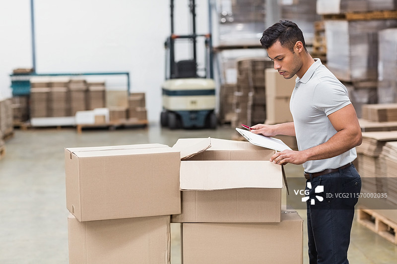 在仓库中检查的男子手持夹板和笔，旁边有叉车和箱子，留有空白空间图片素材