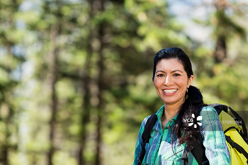 黄色和黑色的背包静静地放在阳光下的郁郁葱葱的松树林中，背景是模糊的松树。图片素材