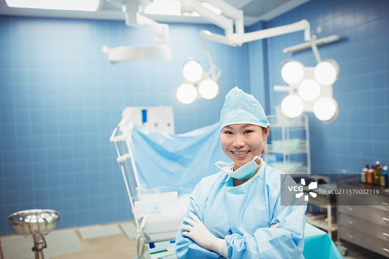 站着的亚洲女性外科医生在手术室中交叉双臂，头顶有灯光，留有空白空间图片素材