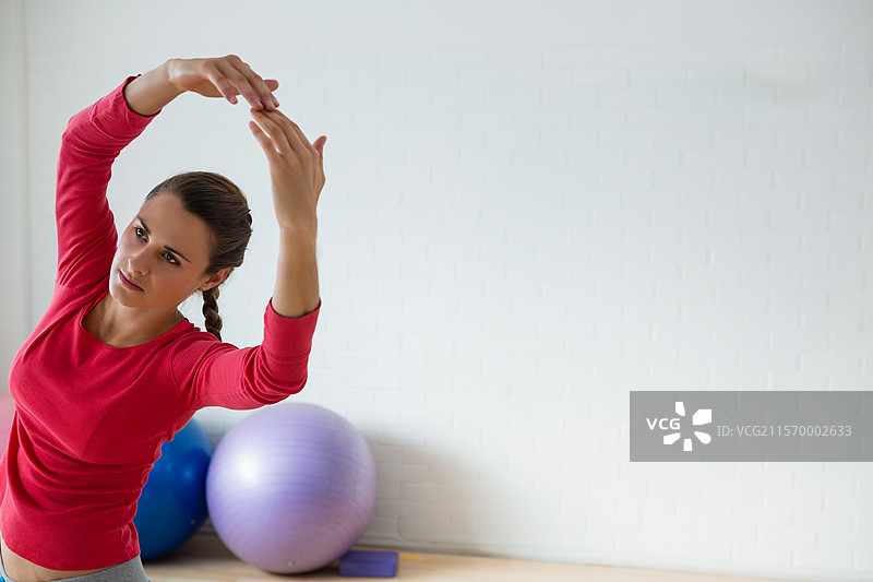 在瑜伽工作室里，侧身伸展的女性，周围有紫色和蓝色的健身球，留有空白空间图片素材