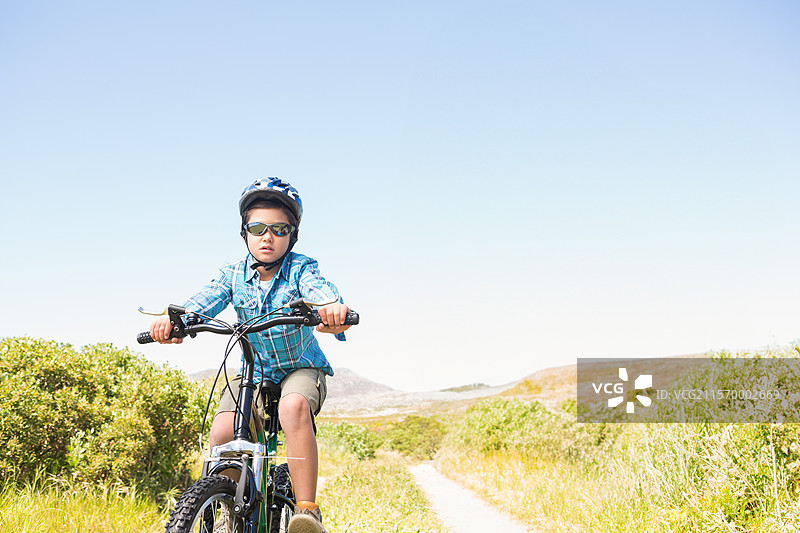 山地自行车在狭窄的泥土小径上行驶，两旁是茂密的绿色灌木，附近是起伏的山丘。图片素材