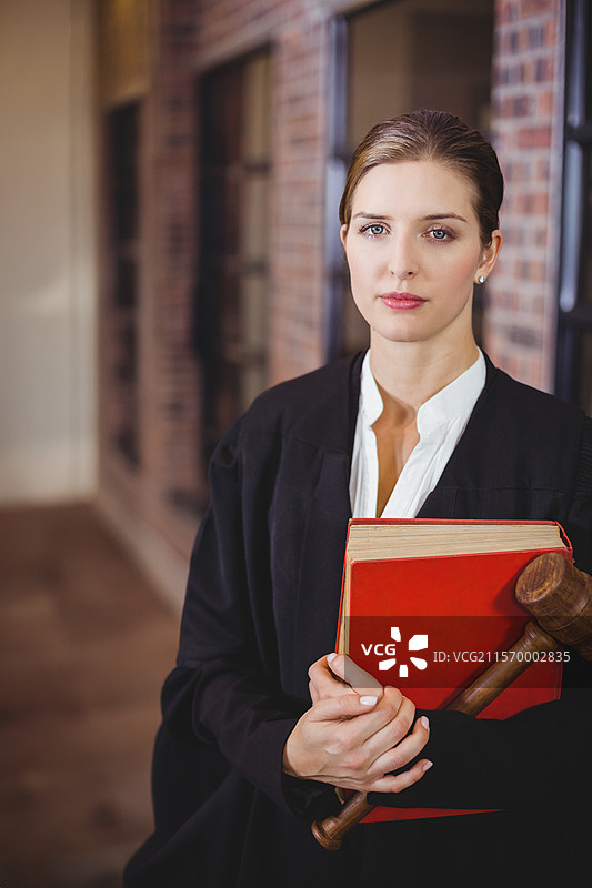 站着的女性在法庭走廊中手持红色法律书和木槌，留有空白空间图片素材